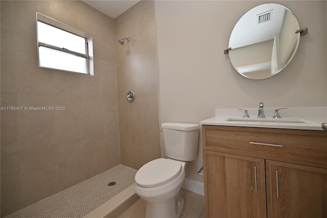 bathroom featuring a tile shower, visible vents, toilet, and vanity