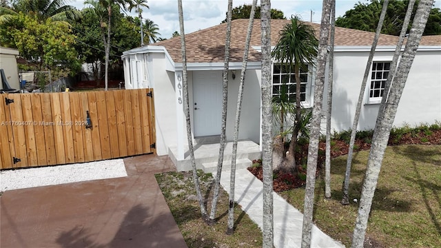 view of side of property with stucco siding, a shingled roof, and fence