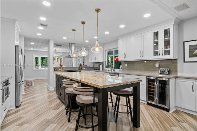 kitchen featuring light wood finished floors, stainless steel appliances, wine cooler, visible vents, and white cabinets