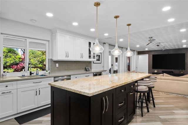 kitchen with dark cabinets, a sink, white cabinets, open floor plan, and a center island