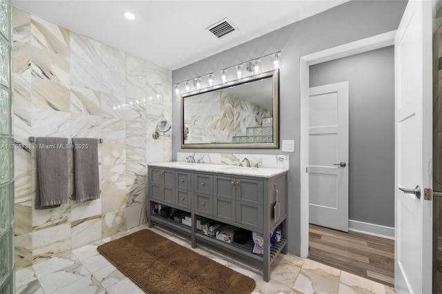 bathroom with a sink, a tile shower, double vanity, and visible vents