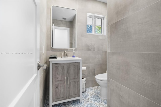 bathroom with tile patterned flooring, visible vents, toilet, vanity, and tile walls