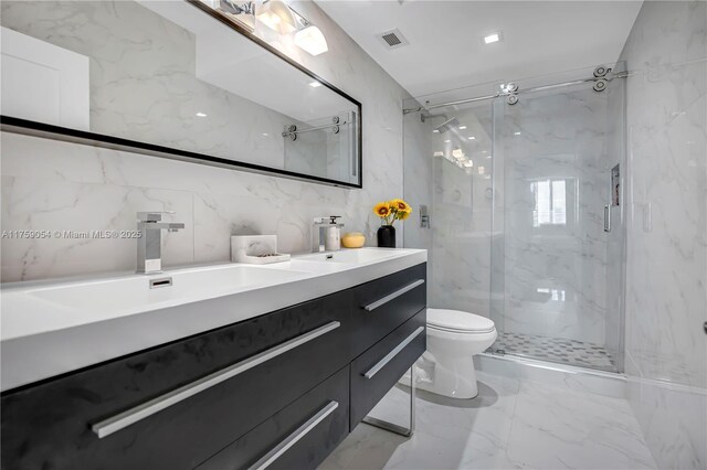 bathroom with a marble finish shower, toilet, double vanity, marble tiled floors, and tile walls