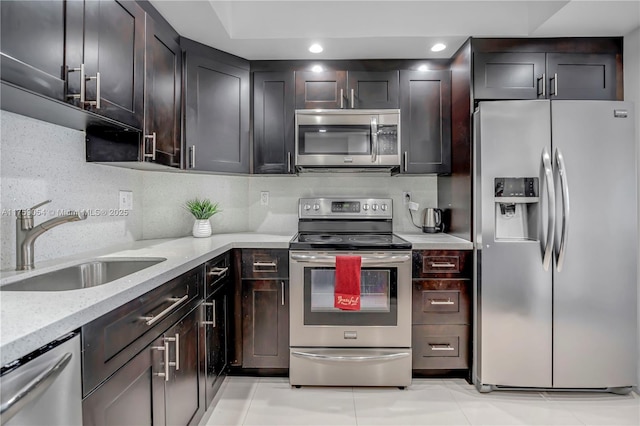 kitchen featuring light stone countertops, light tile patterned flooring, a sink, appliances with stainless steel finishes, and backsplash