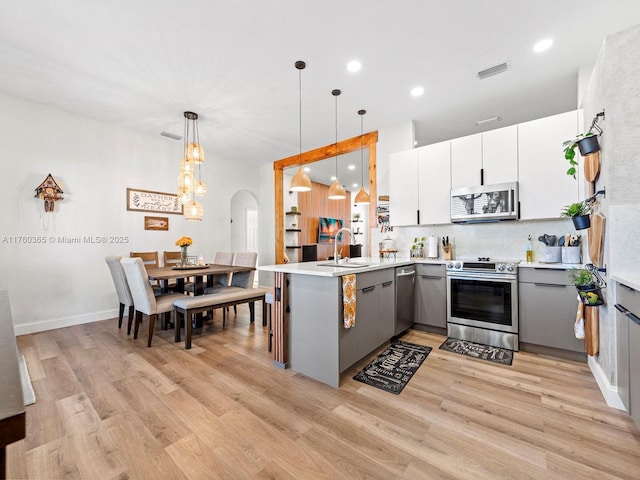 kitchen featuring visible vents, a peninsula, gray cabinets, a sink, and appliances with stainless steel finishes