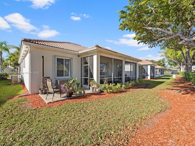 rear view of property with a sunroom, central AC, stucco siding, a tiled roof, and a lawn