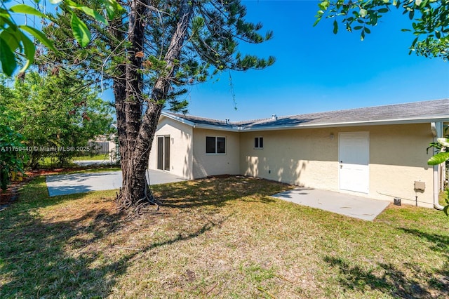 back of property with a patio area, stucco siding, and a yard