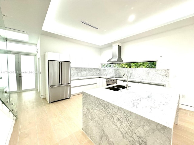 kitchen featuring a sink, a raised ceiling, wall chimney exhaust hood, and freestanding refrigerator