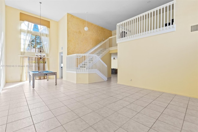 unfurnished living room featuring tile patterned flooring, stairway, pool table, and a high ceiling