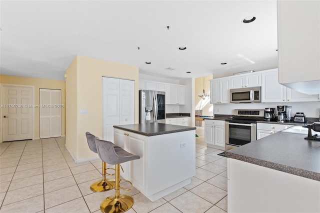 kitchen with light tile patterned floors, stainless steel appliances, white cabinets, dark countertops, and a center island