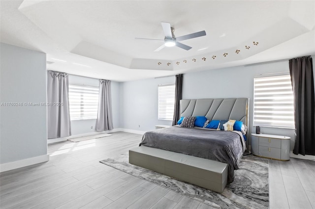 bedroom featuring multiple windows, a raised ceiling, baseboards, and light wood finished floors