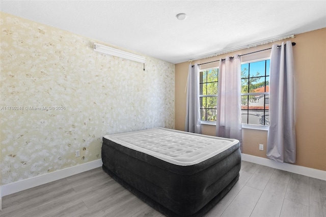 bedroom featuring wallpapered walls, wood finished floors, and baseboards