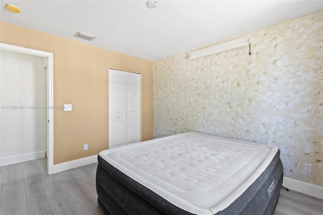 bedroom with a closet, visible vents, baseboards, and wood finished floors