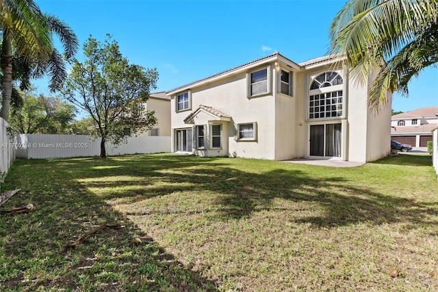 rear view of property featuring a yard, fence, and stucco siding