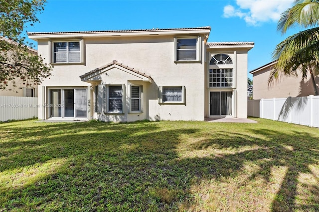 rear view of house featuring a lawn, a tiled roof, a fenced backyard, and stucco siding