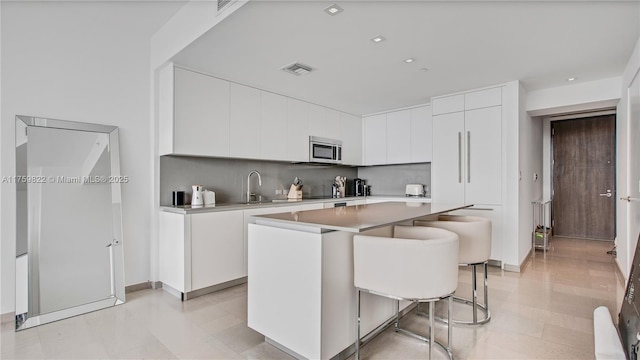 kitchen featuring visible vents, modern cabinets, stainless steel microwave, a center island, and white cabinets