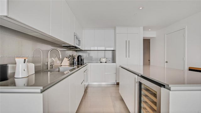 kitchen with beverage cooler, a kitchen island, a sink, stainless steel microwave, and modern cabinets