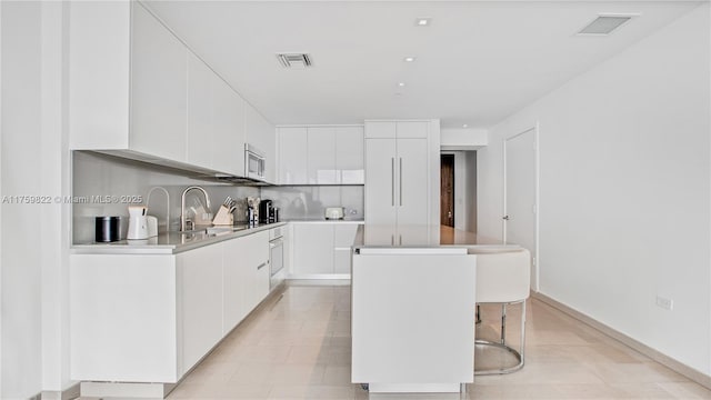 88 SW 7th St Unit 2208, Miami, FL 33130 - kitchen featuring stainless steel microwave, a kitchen island, modern cabinets, and white cabinets