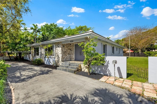 single story home with stone siding, stucco siding, a front yard, and fence