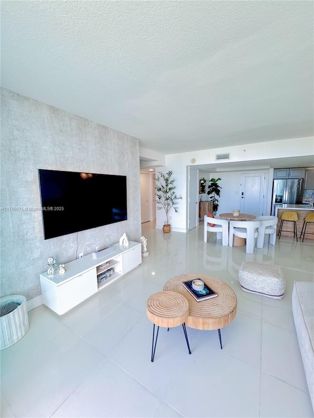 tiled living area with an accent wall, baseboards, visible vents, and a textured ceiling