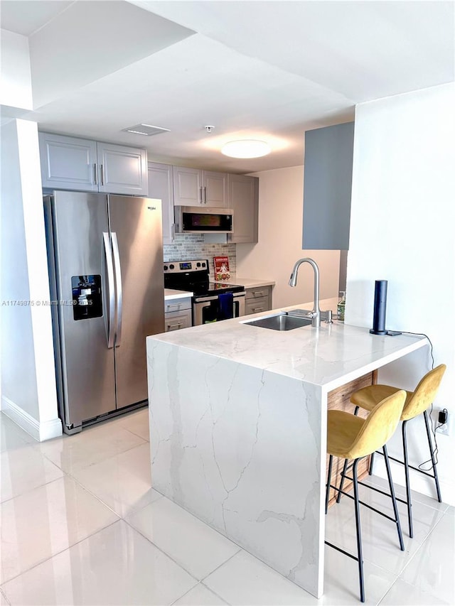 kitchen featuring light stone counters, gray cabinets, a peninsula, stainless steel appliances, and a sink