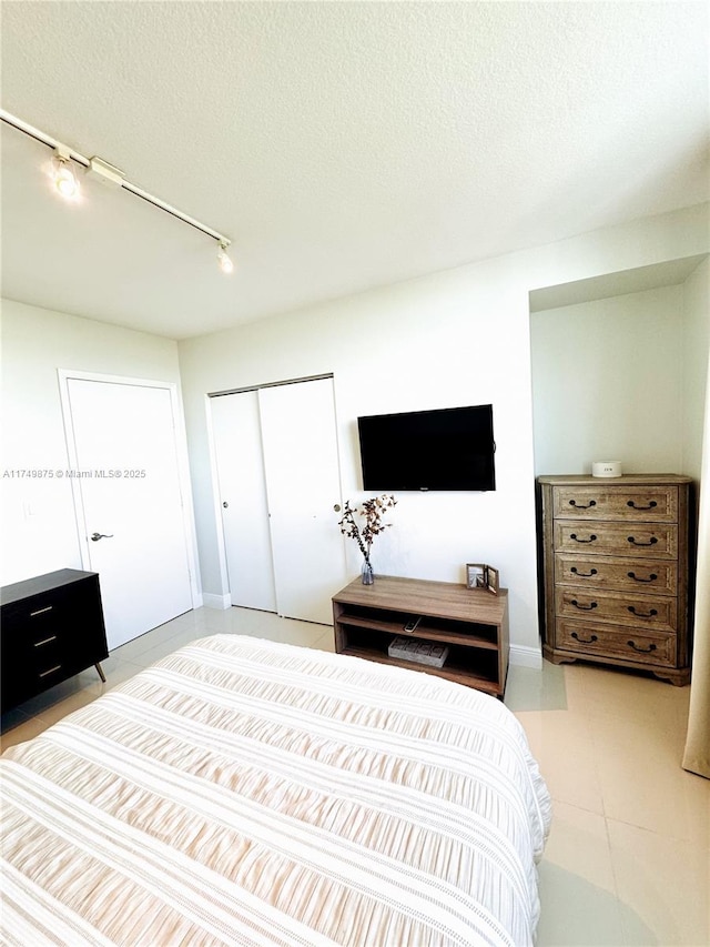 bedroom with light tile patterned floors, a closet, a textured ceiling, and track lighting