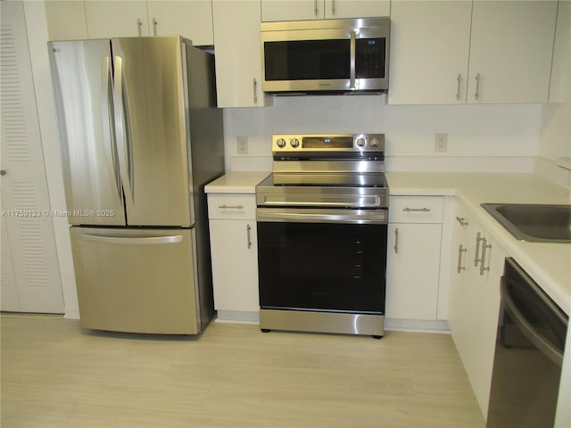 kitchen with light wood-type flooring, white cabinets, stainless steel appliances, and light countertops