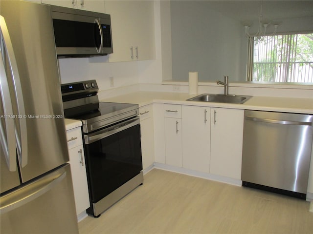 kitchen featuring a sink, appliances with stainless steel finishes, white cabinets, light wood finished floors, and light countertops