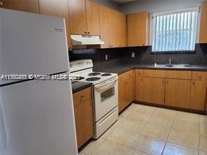 kitchen with dark countertops, under cabinet range hood, freestanding refrigerator, white electric range oven, and a sink