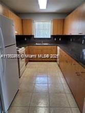 kitchen with a sink, dark countertops, light tile patterned floors, and stainless steel appliances