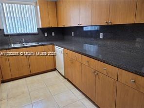 kitchen featuring light tile patterned flooring, white dishwasher, a sink, decorative backsplash, and dark countertops