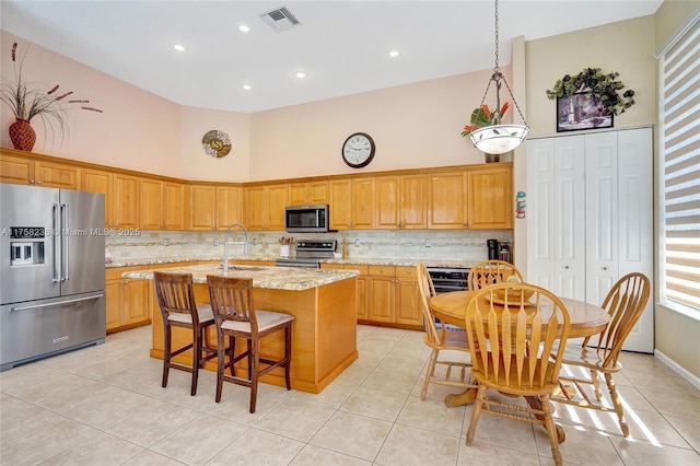 kitchen with visible vents, a high ceiling, an island with sink, a sink, and appliances with stainless steel finishes