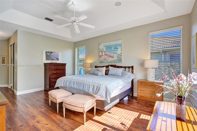 bedroom featuring visible vents, a ceiling fan, wood finished floors, baseboards, and a raised ceiling