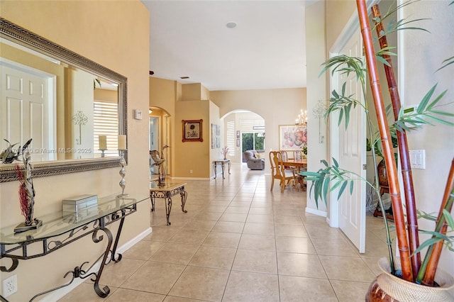 foyer with a notable chandelier, light tile patterned floors, baseboards, and arched walkways