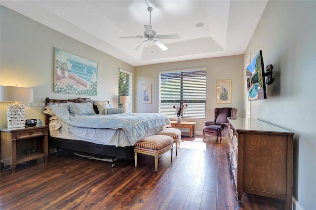 bedroom featuring a raised ceiling, baseboards, dark wood-type flooring, and ceiling fan