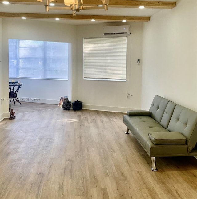 living area with an AC wall unit, wood finished floors, baseboards, and beam ceiling