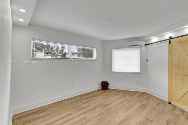 unfurnished bedroom with light wood finished floors, baseboards, an AC wall unit, a barn door, and recessed lighting