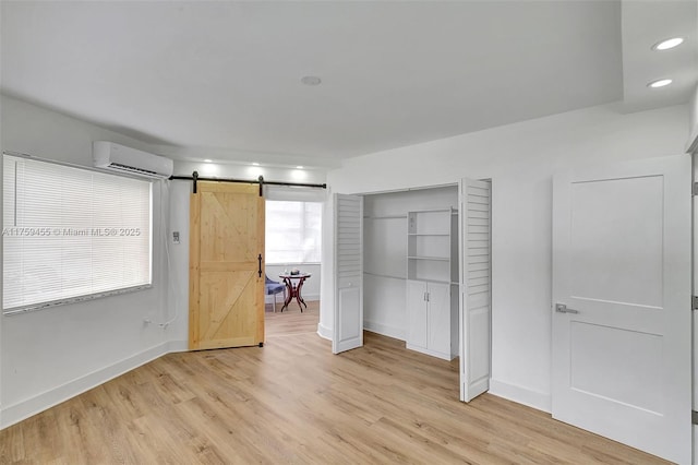 unfurnished bedroom with a wall unit AC, baseboards, light wood finished floors, a closet, and a barn door