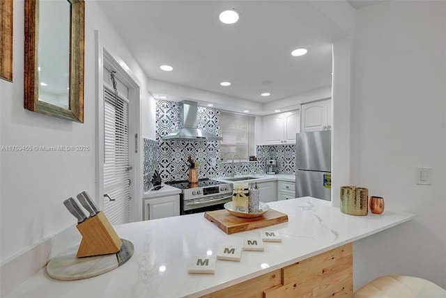 kitchen with a sink, decorative backsplash, stainless steel appliances, white cabinets, and wall chimney range hood