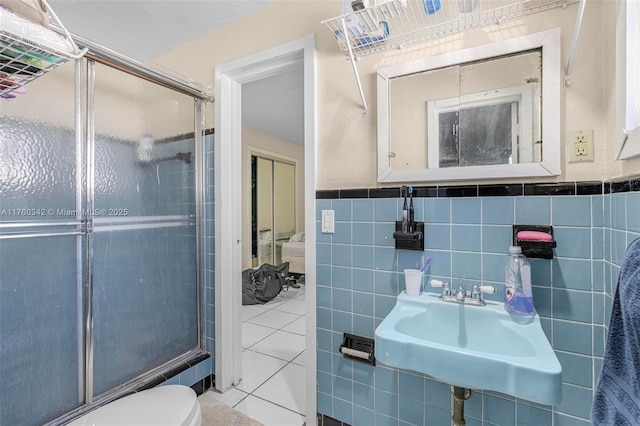 full bath featuring a wainscoted wall, toilet, a stall shower, tile walls, and a sink