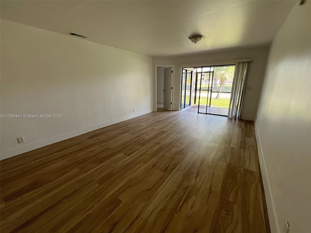 empty room featuring wood finished floors, visible vents, and baseboards