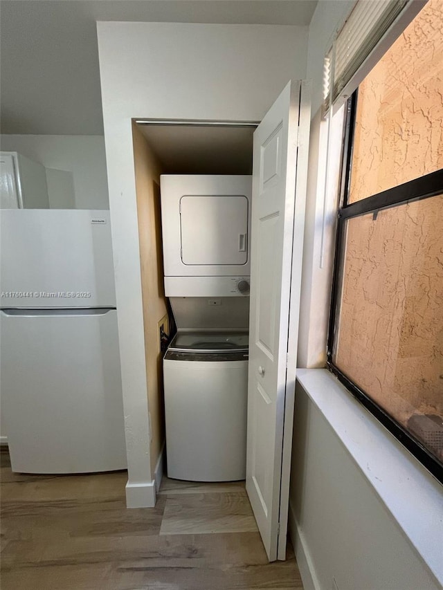 clothes washing area with wood finished floors, baseboards, and stacked washer and dryer