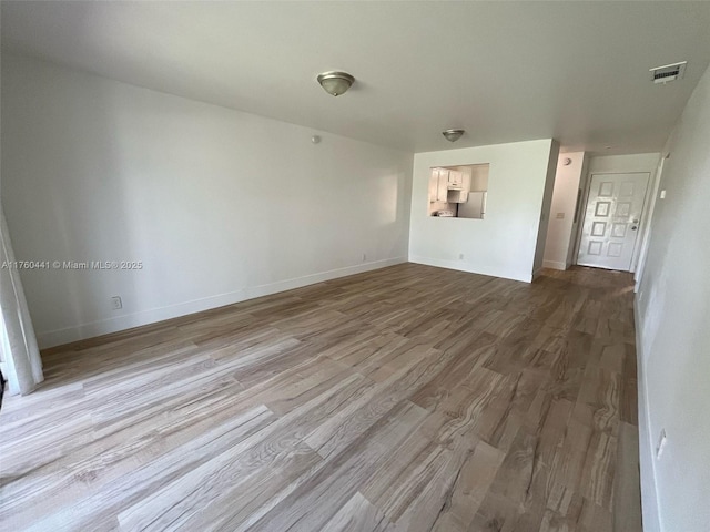 empty room with wood finished floors, visible vents, and baseboards