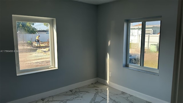 spare room featuring marble finish floor, baseboards, and a wealth of natural light