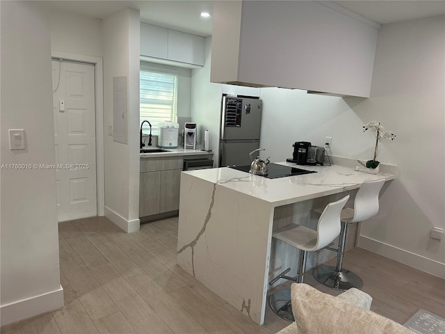 kitchen with a sink, fridge, a peninsula, a breakfast bar area, and black electric cooktop