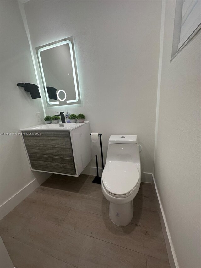 half bathroom featuring toilet, vanity, baseboards, and wood finished floors