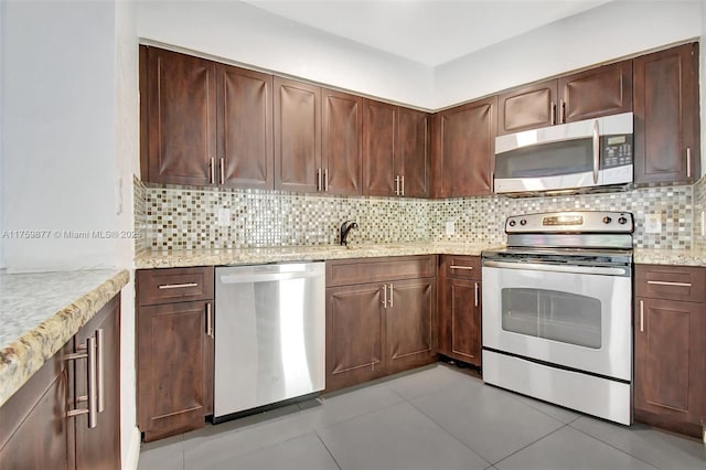 kitchen with a sink, backsplash, stainless steel appliances, light tile patterned flooring, and light stone countertops