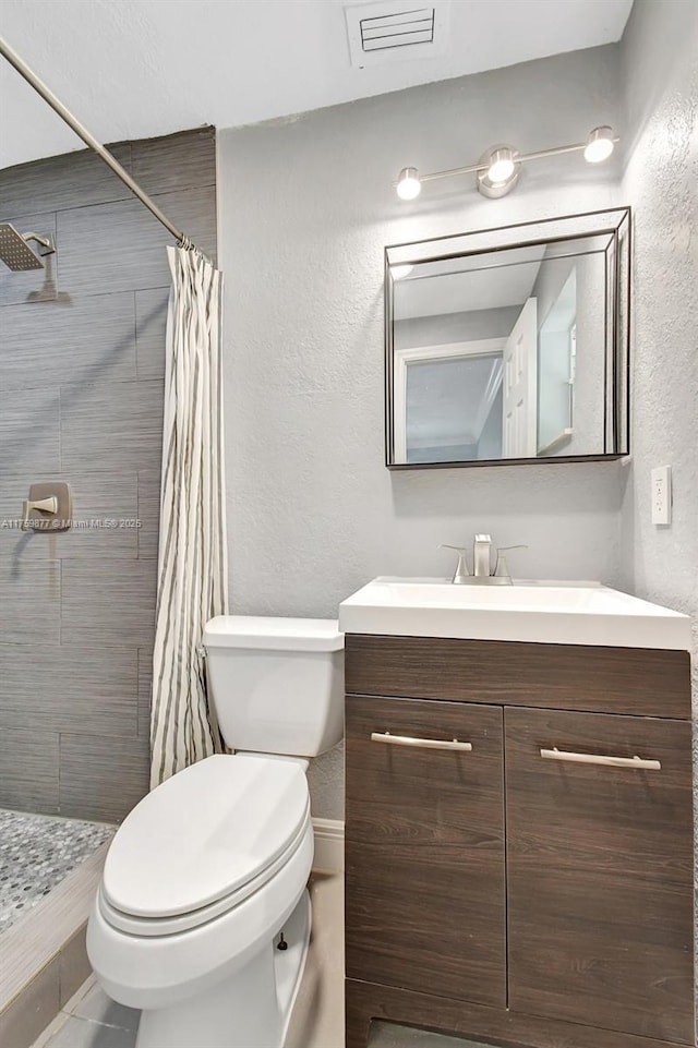 full bath with visible vents, tiled shower, toilet, and vanity