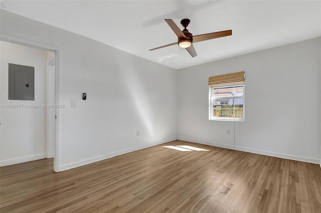 spare room with electric panel, light wood-style flooring, a ceiling fan, and baseboards