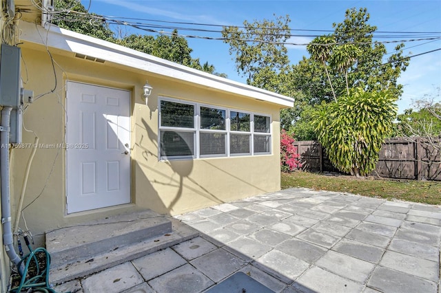 property entrance featuring a patio area, fence, and stucco siding